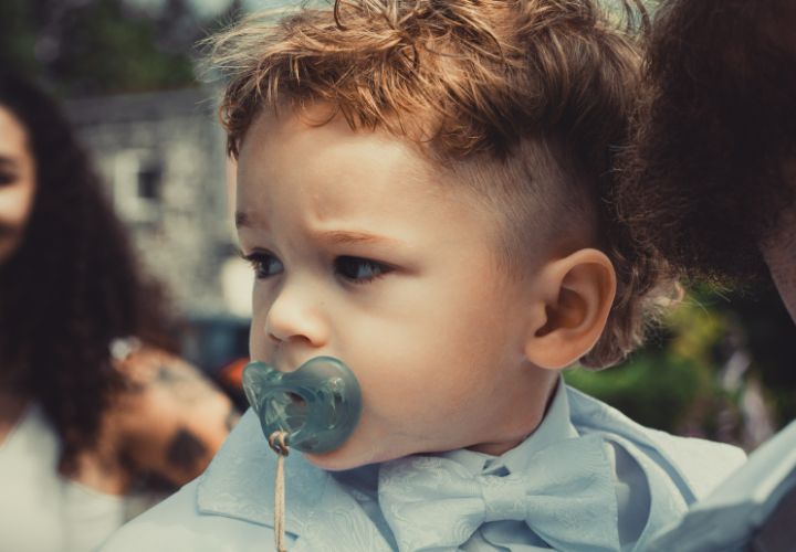 Enfant en habit propre avec une sucette dans la bouche.